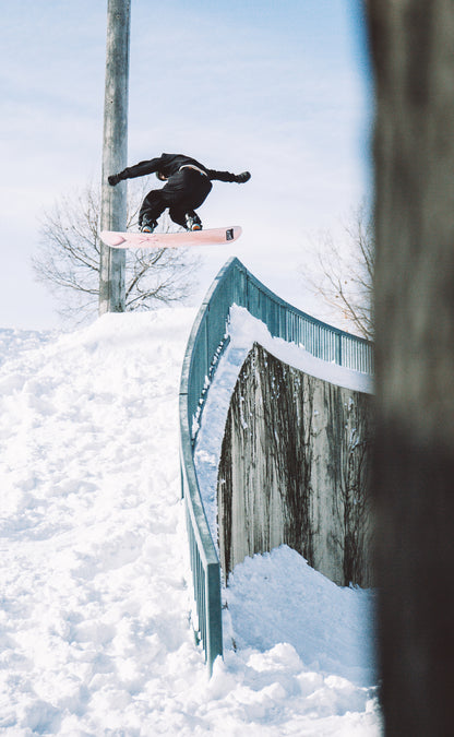 Snowboarder performing trick on SLEEP PINK CLOUD PRO board over snowy rail in winter scene.