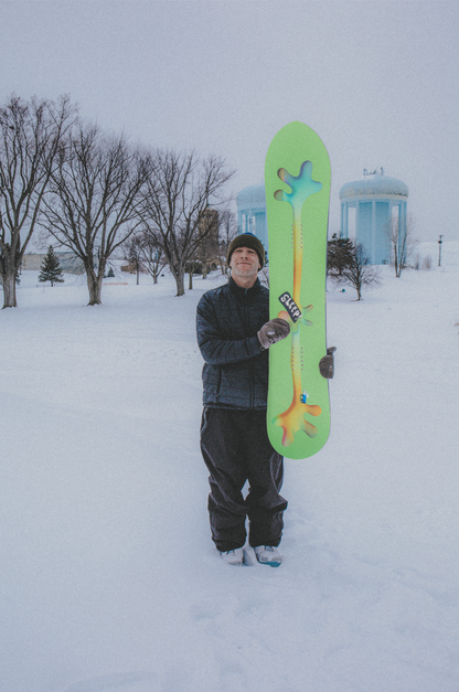 Person holding vibrant snow-green Sleep Hitch Hiker snowboard in snowy landscape.