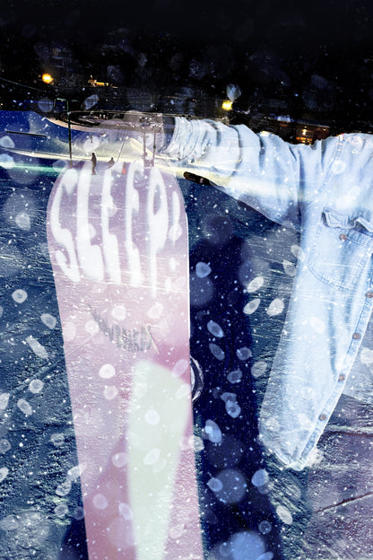 Snowboarder holds Sleep Jibby 147 snowboard in snowy night scene, showcasing the board's design and performance quality.