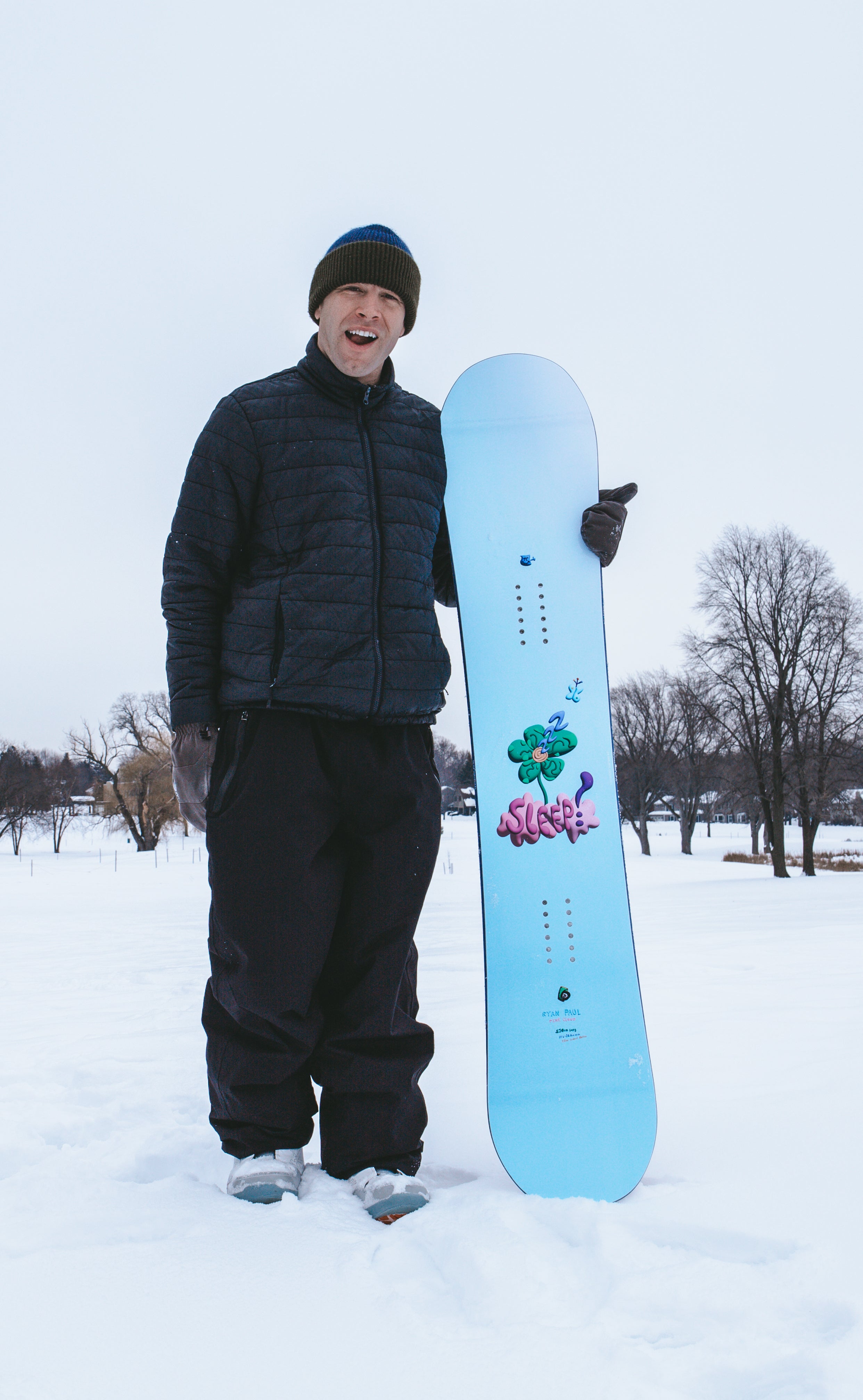 Person standing with a SLEEP PINK CLOUD PRO SNOWBOARD 150 in a snowy landscape, showcasing the board's design and features.